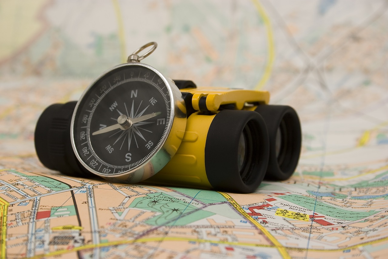 paper map topped with a compass leaning against a pair of small yellow binoculars